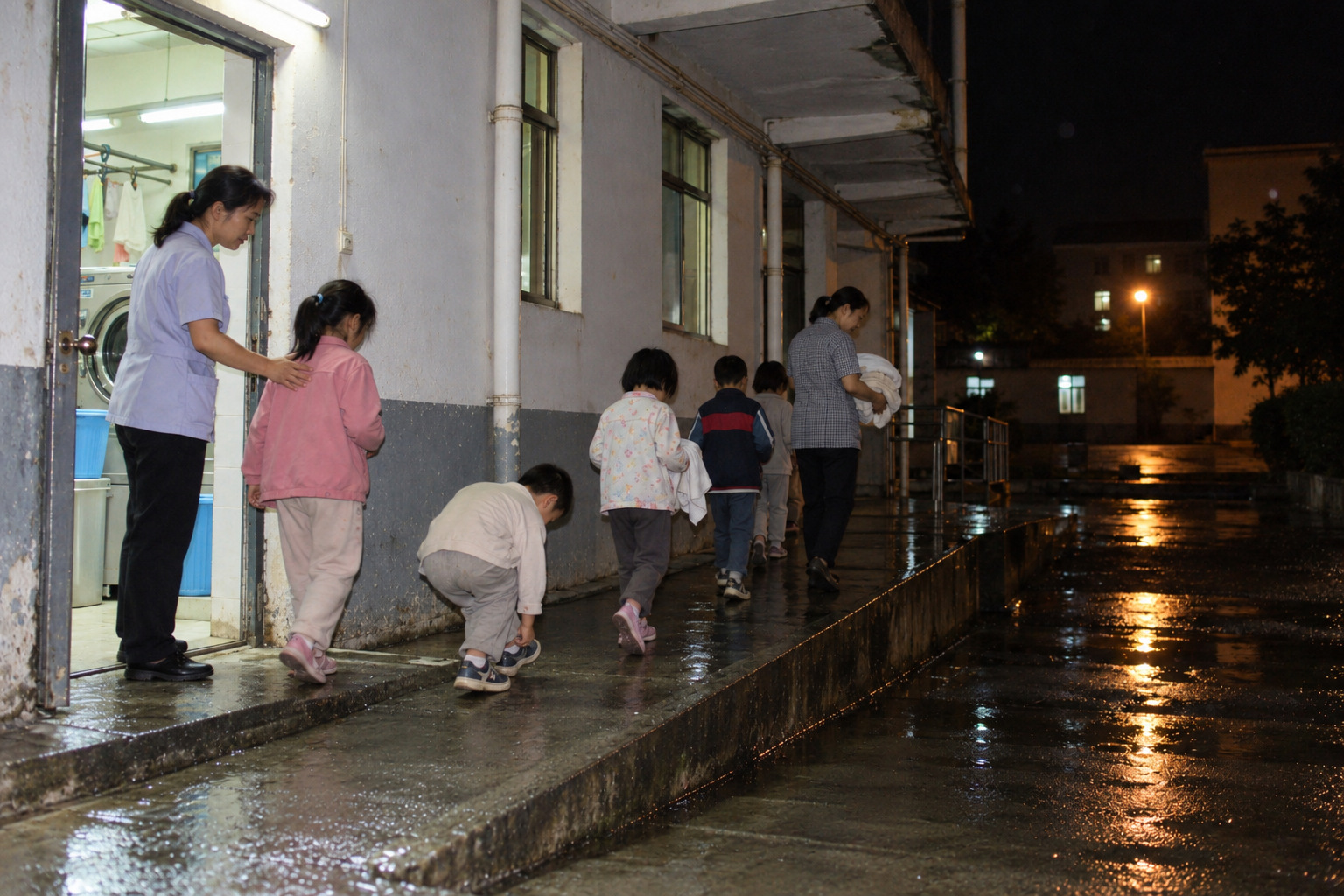 夜里老师在后门引导穿干衣的孩子靠墙走过坡道。